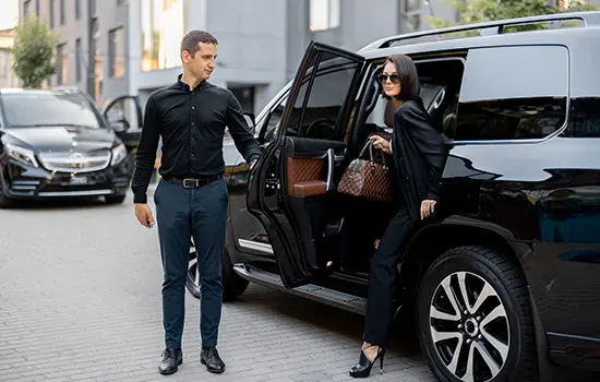 A chauffeur holds the door of a black SUV open for a passenger